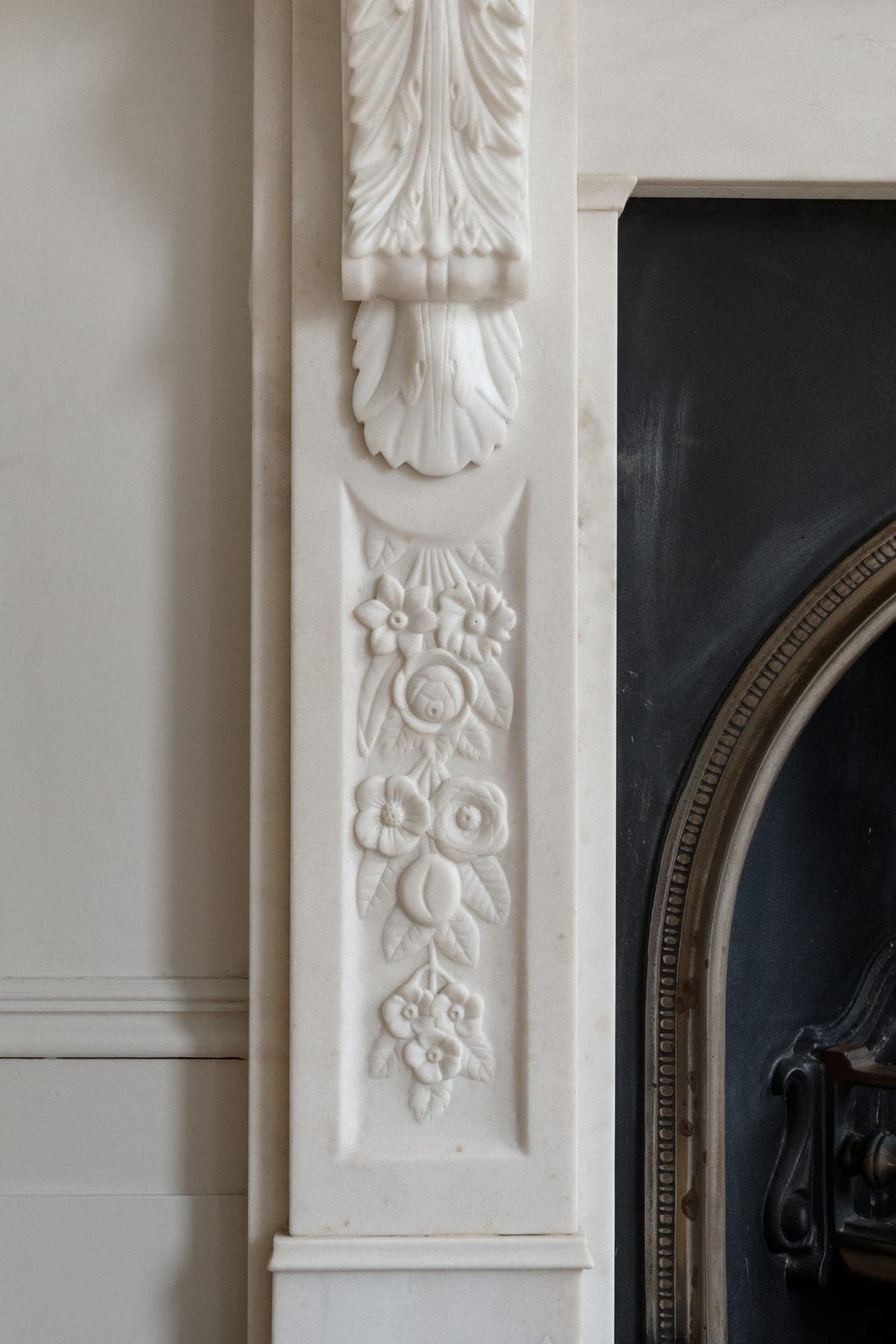 Carved white marble fireplace detail with floral relief and arched cast-iron grate