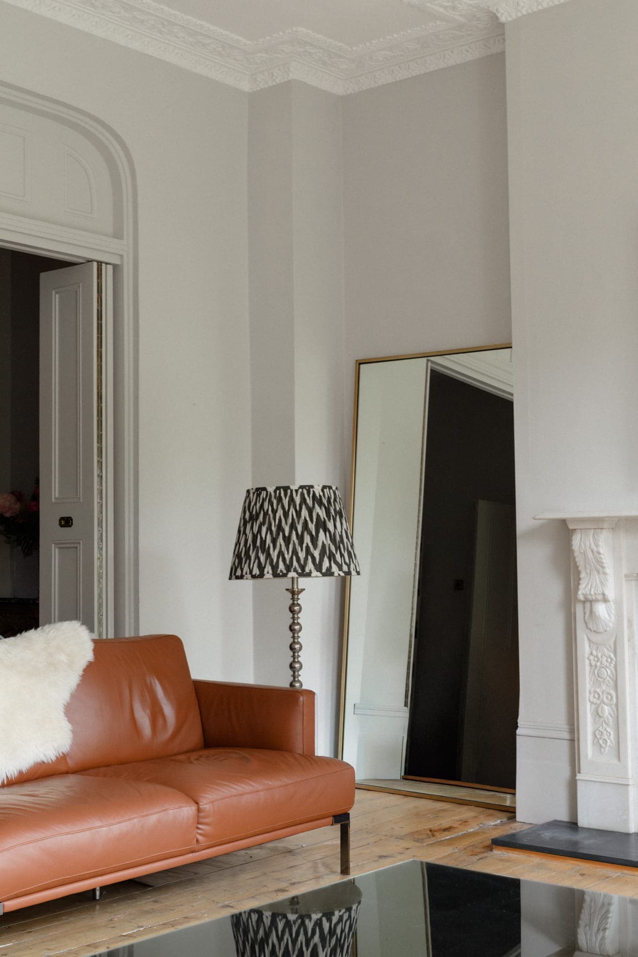 Sunlit London living room with tan leather sofa, full-length mirror and ornate plasterwork